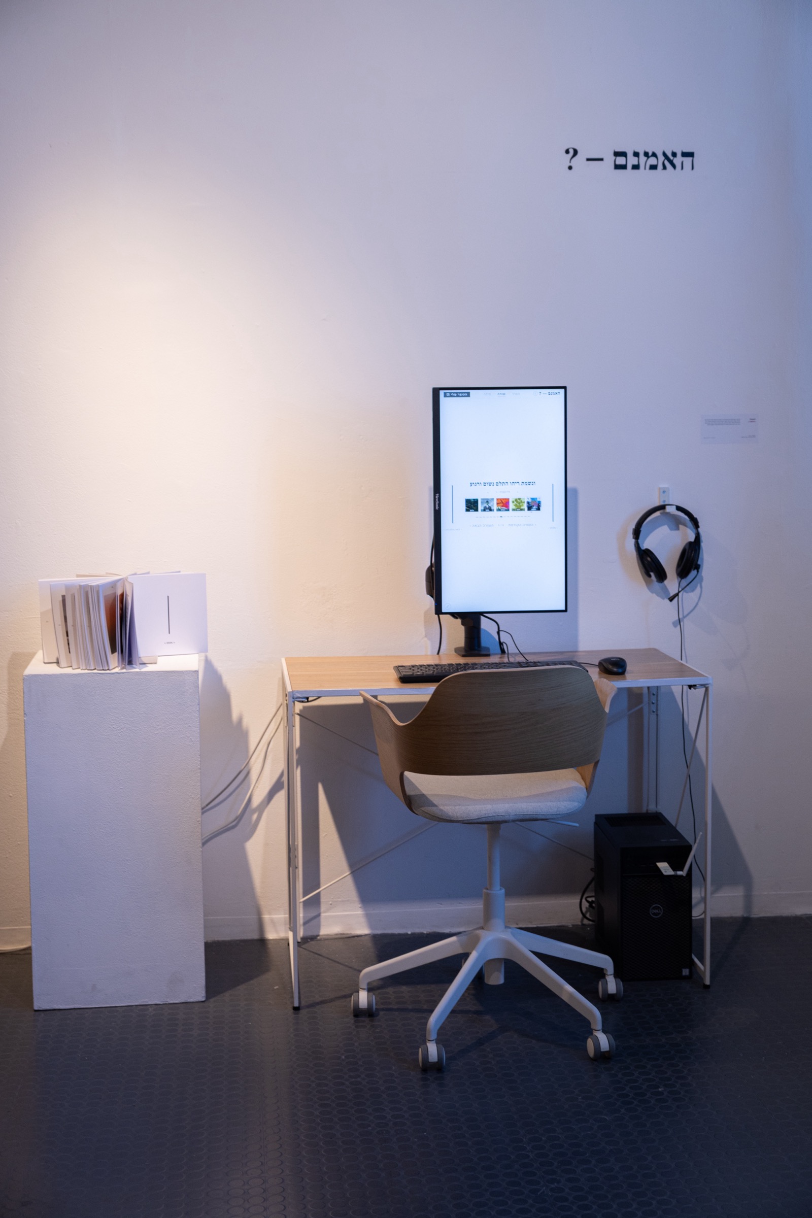 האמנם — ? installed: the portrait kiosk, headphones, and the printed book in the exhibition space.