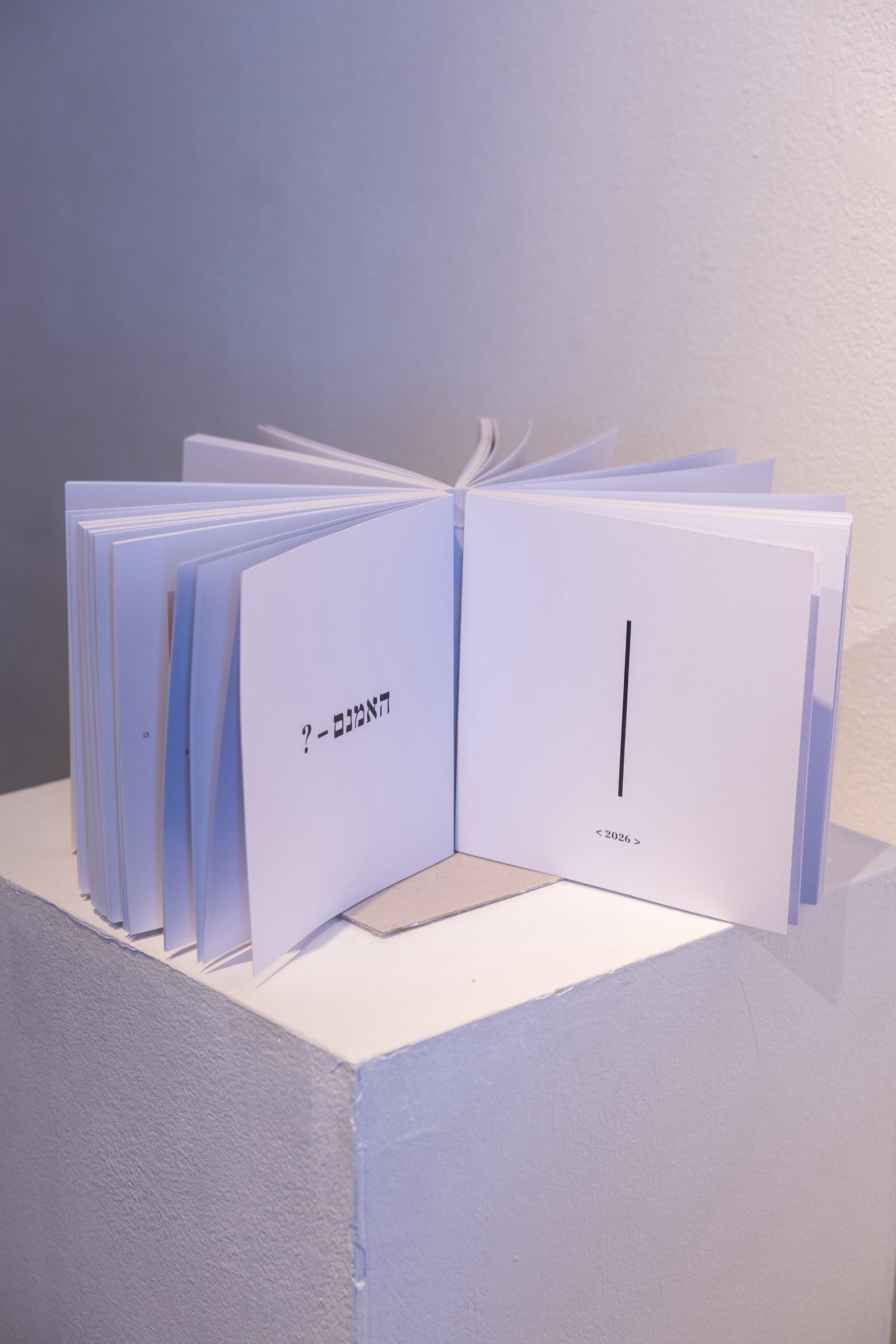 The book standing open at its title spread on the plinth: האמנם — ?